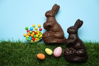 Chocolate Easter bunnies, eggs and candies with green grass on light blue background