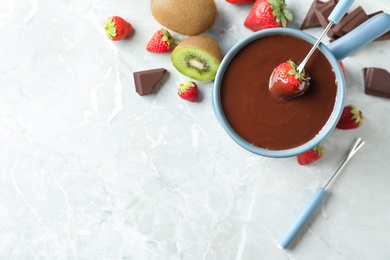 Photo of Dipping strawberry into fondue pot with chocolate on light grey marble table, flat lay. Space for text