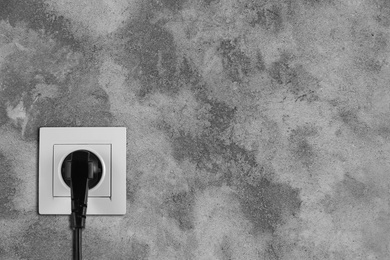 Image of Stone wall with power socket and inserted plug, space for text. Electrical supply