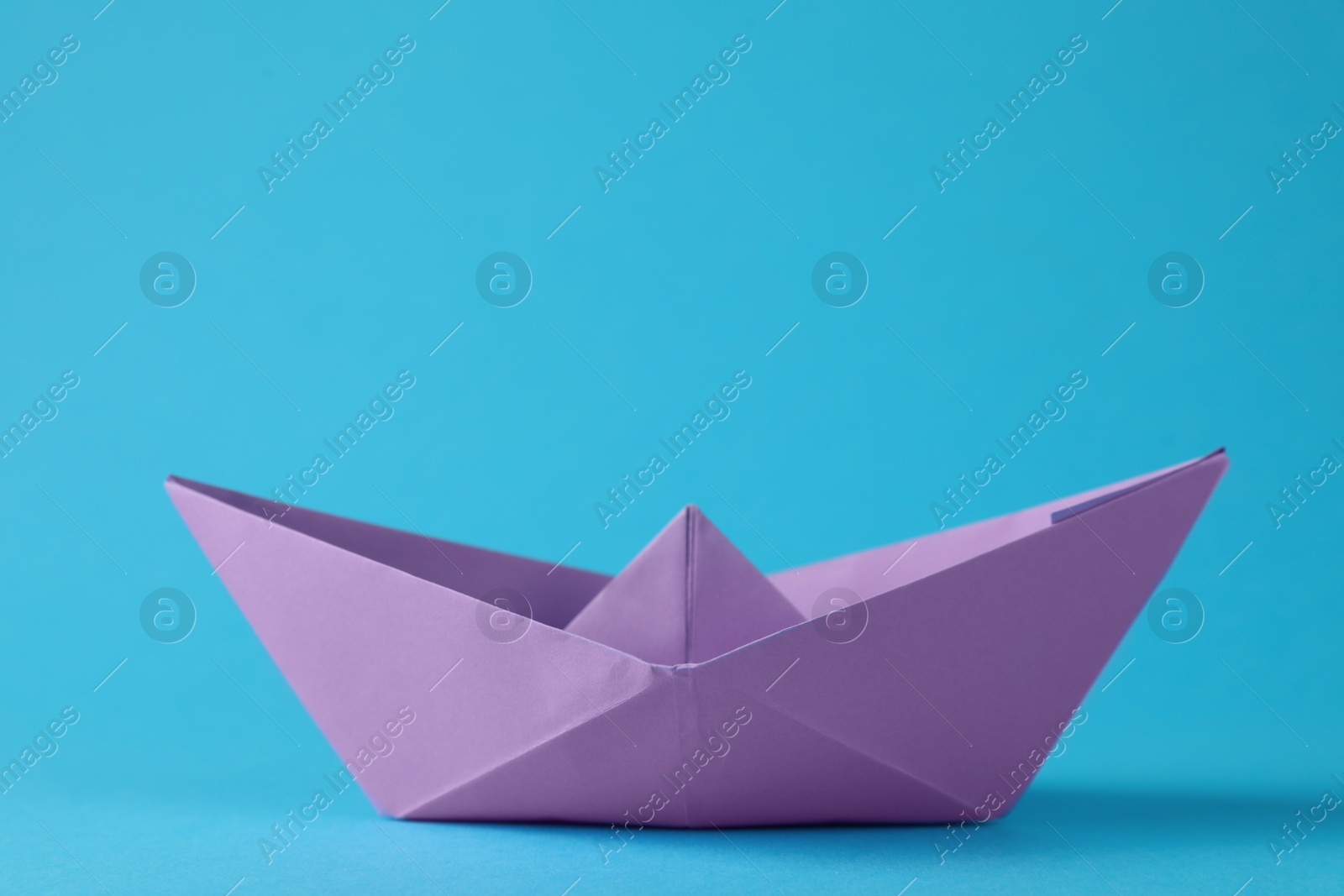 Photo of Handmade violet paper boat on light blue background. Origami art
