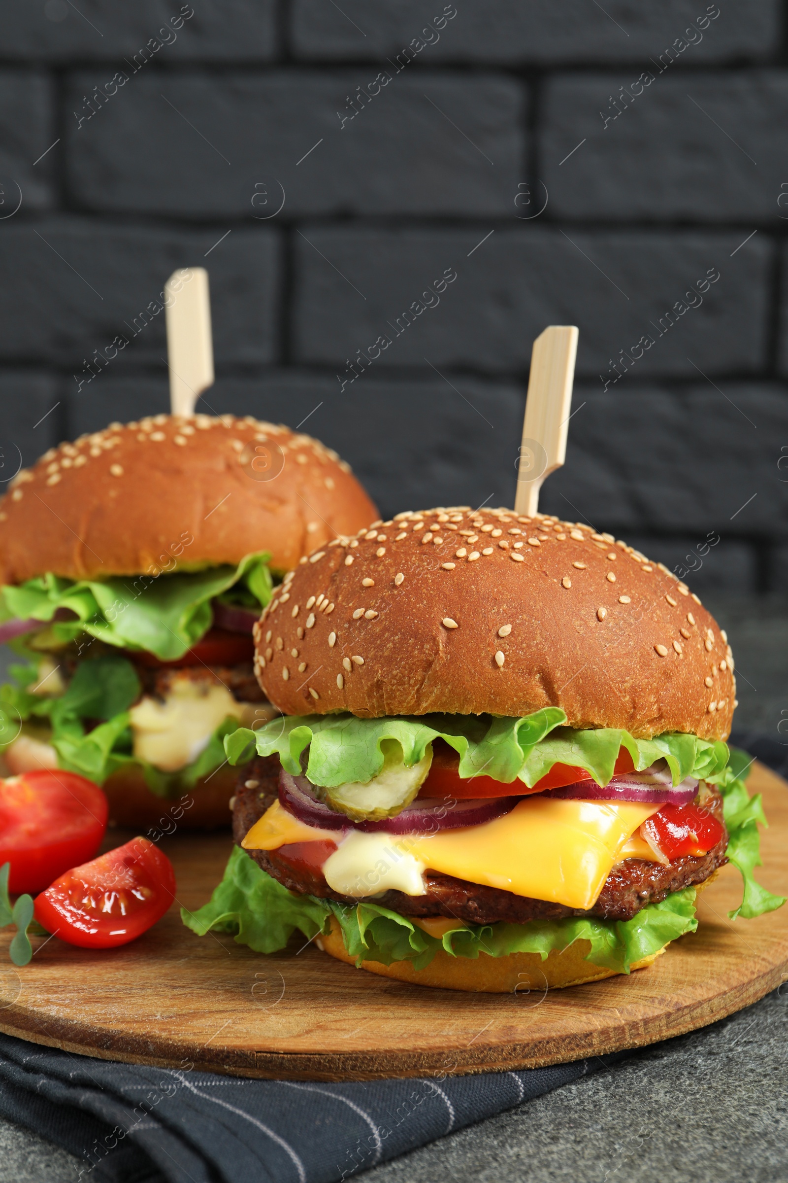 Photo of Delicious burgers with beef patty and tomatoes on grey table