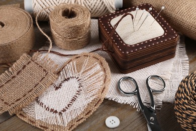 Photo of Pieces of burlap fabric with different stitches, scissors, twine and pincushion on wooden table, closeup