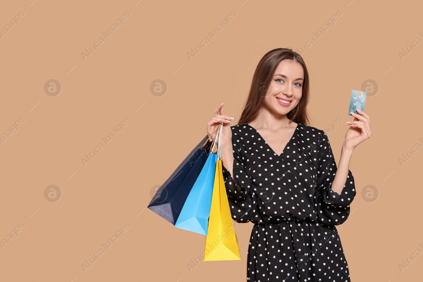 Photo of Stylish young woman with shopping bags and credit card on beige background, space for text