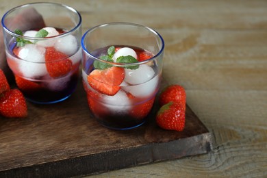 Photo of Delicious cocktails with strawberries, mint and ice balls on wooden table