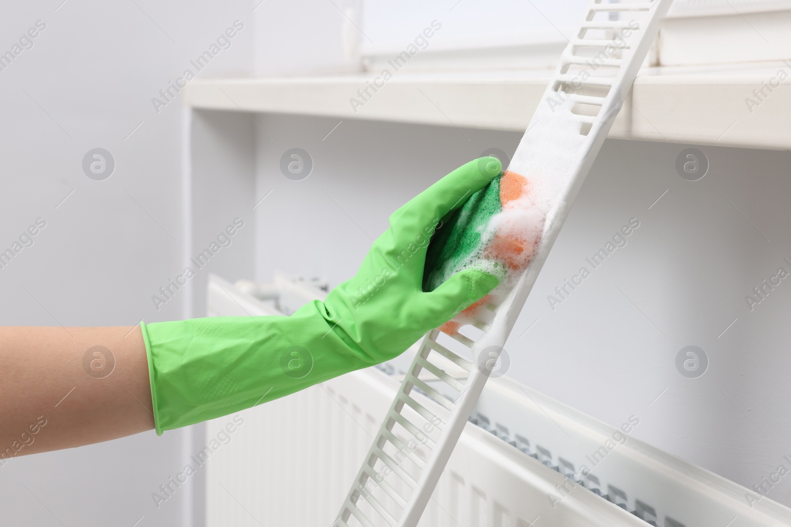 Photo of Woman washing radiator grill with sponge and detergent indoors, closeup