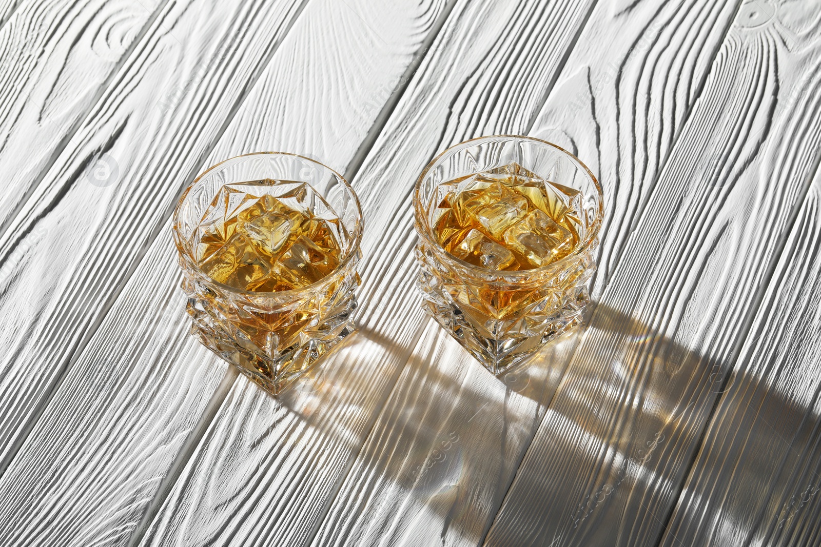 Photo of Whiskey with ice cubes in glasses on white wooden table