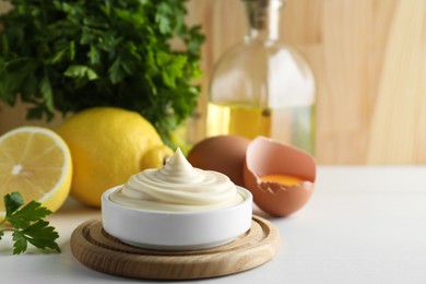 Photo of Fresh mayonnaise sauce in bowl and ingredients on white wooden table, space for text