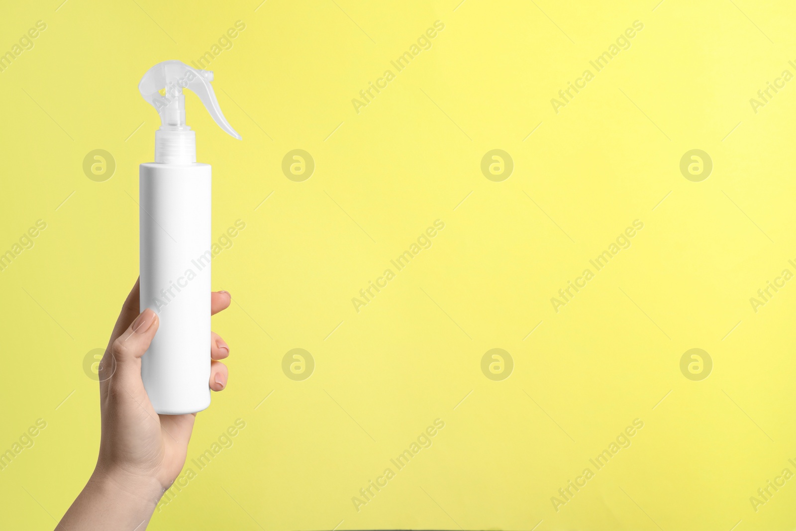 Photo of Woman holding spray bottle with hair thermal protection against pale yellow background, closeup. Space for text