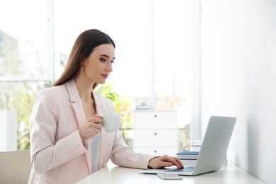 Young woman drinking coffee while working on laptop in office