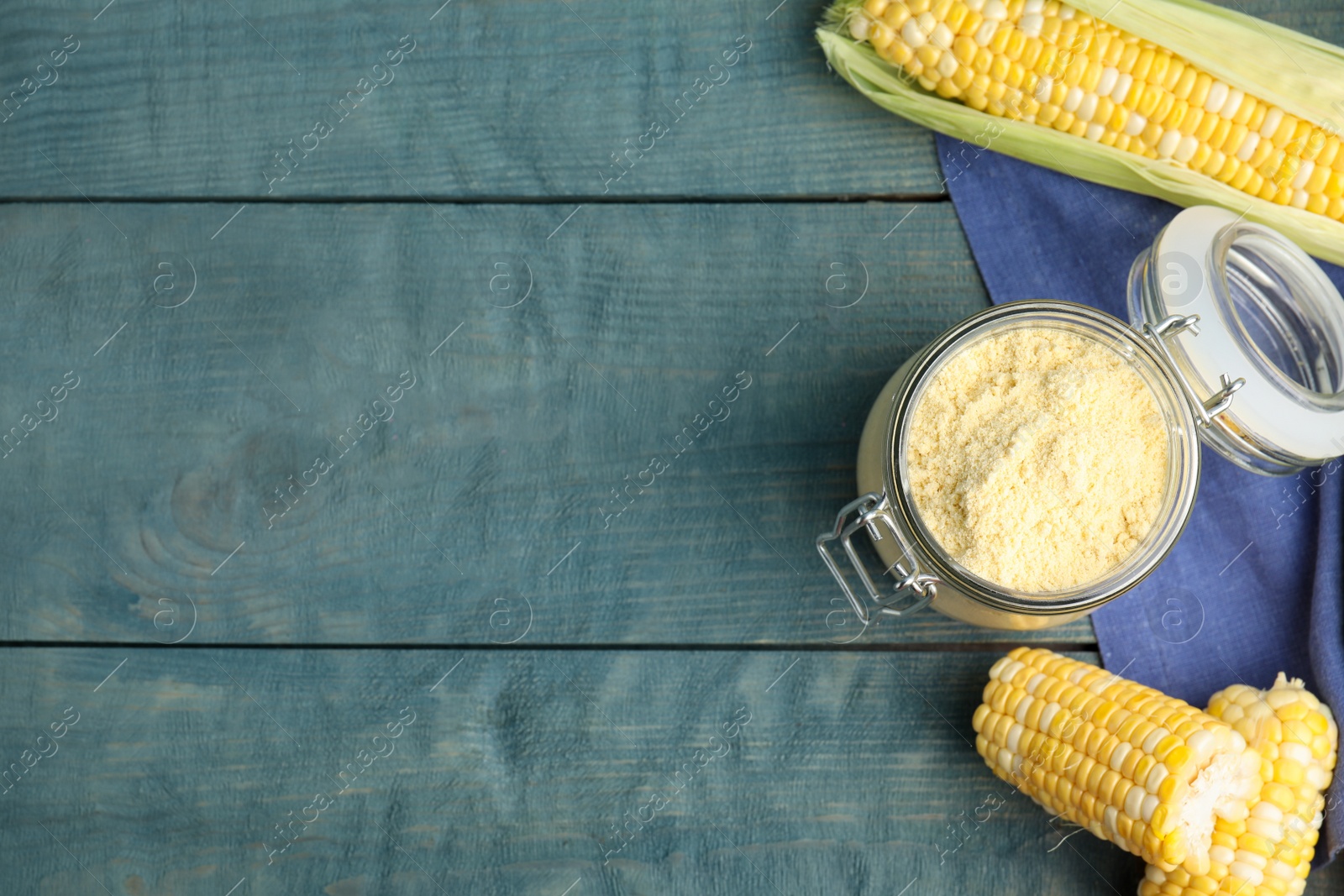 Photo of Corn flour in glass jar and fresh cobs on blue wooden table, flat lay. Space for text