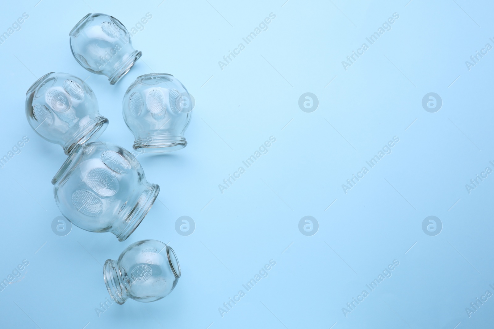 Photo of Many glass cups on light blue background, flat lay with space for text. Cupping therapy