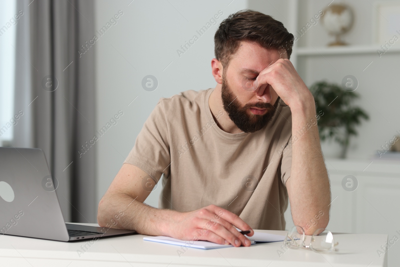 Photo of Overwhelmed man sitting with laptop at table indoors