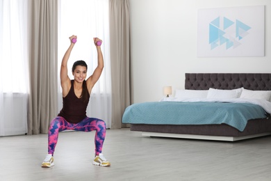 Photo of Young woman in fitness clothes doing exercise with dumbbells at home. Space for text