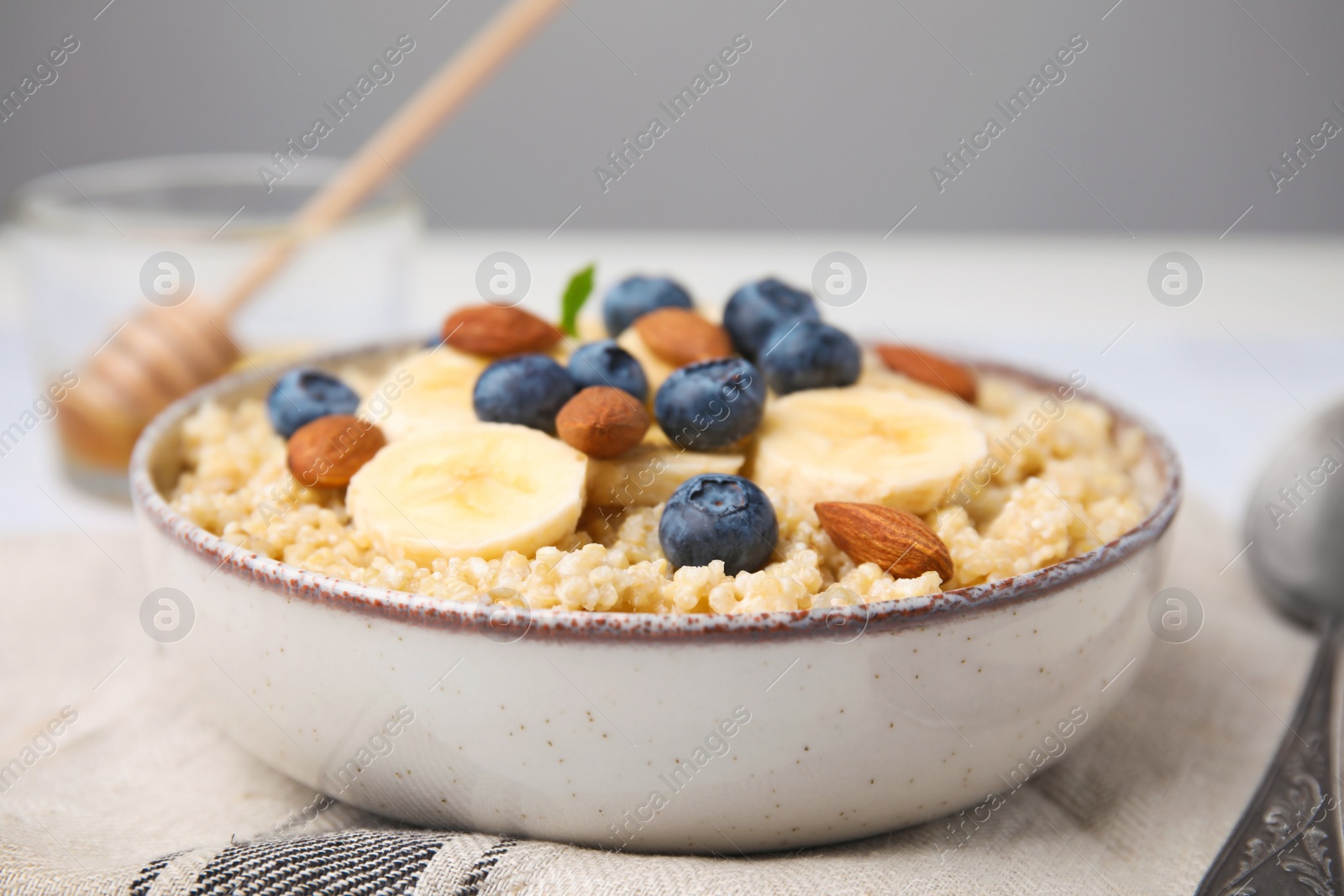 Photo of Bowl of delicious cooked quinoa with almonds, bananas and blueberries on kitchen towel, closeup