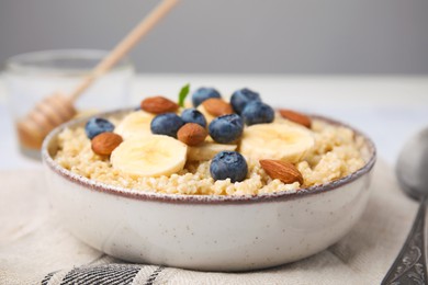 Bowl of delicious cooked quinoa with almonds, bananas and blueberries on kitchen towel, closeup