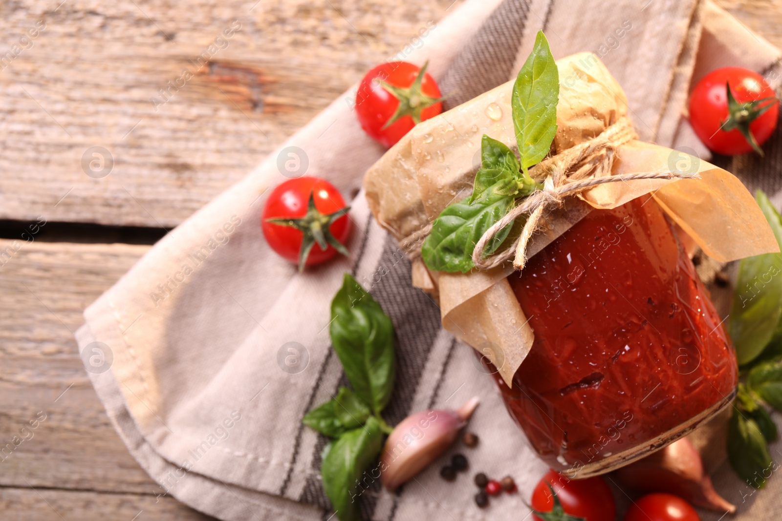 Photo of Jar of tasty tomato paste with water drops and ingredients on wooden table, flat lay. Space for text