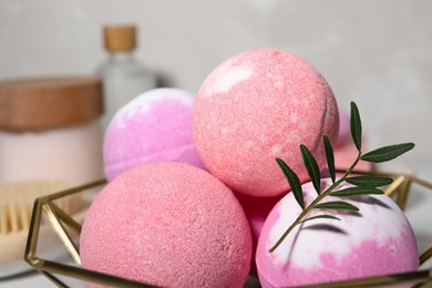 Photo of Beautiful aromatic bath bombs and green twig in decorative bowl on blurred background, closeup