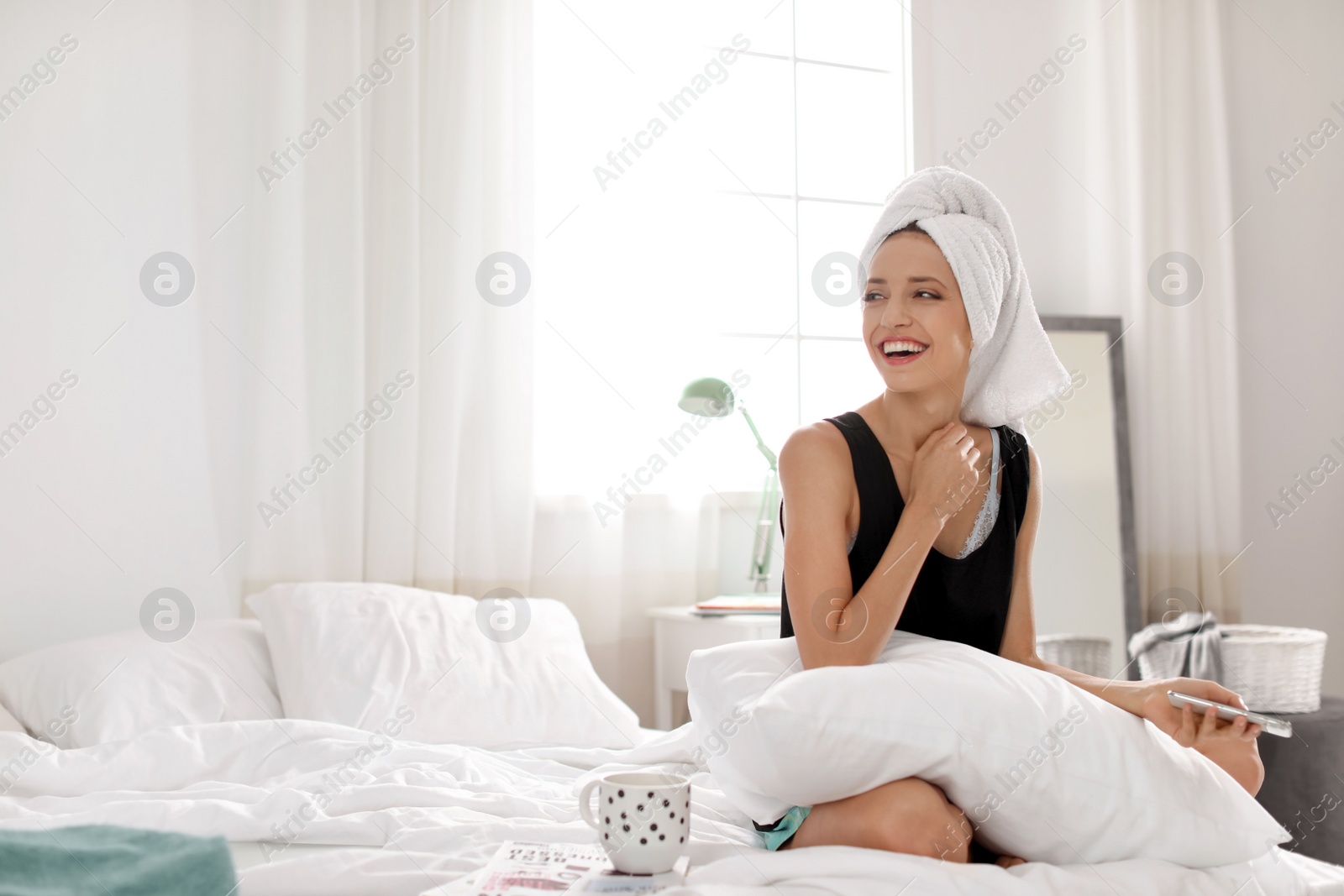 Photo of Young happy woman with mobile phone on bed at home. Lazy morning