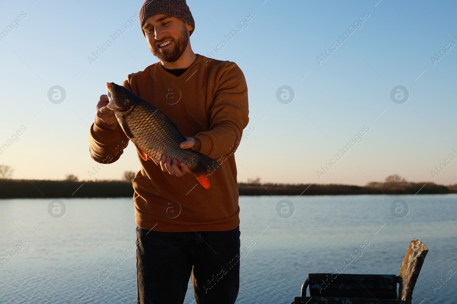 Photo of Fisherman holding caught fish at riverside. Recreational activity