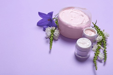 Photo of Jars of body cream and flowers on lilac background. Space for text