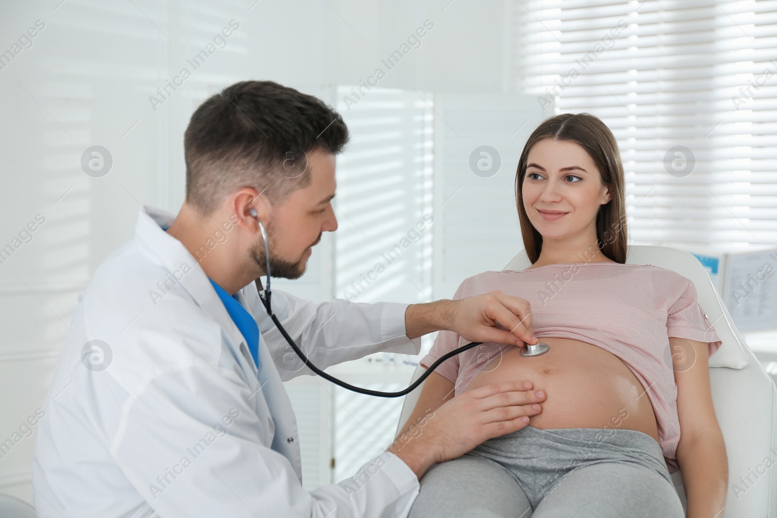 Photo of Doctor examining pregnant woman with stethoscope in clinic