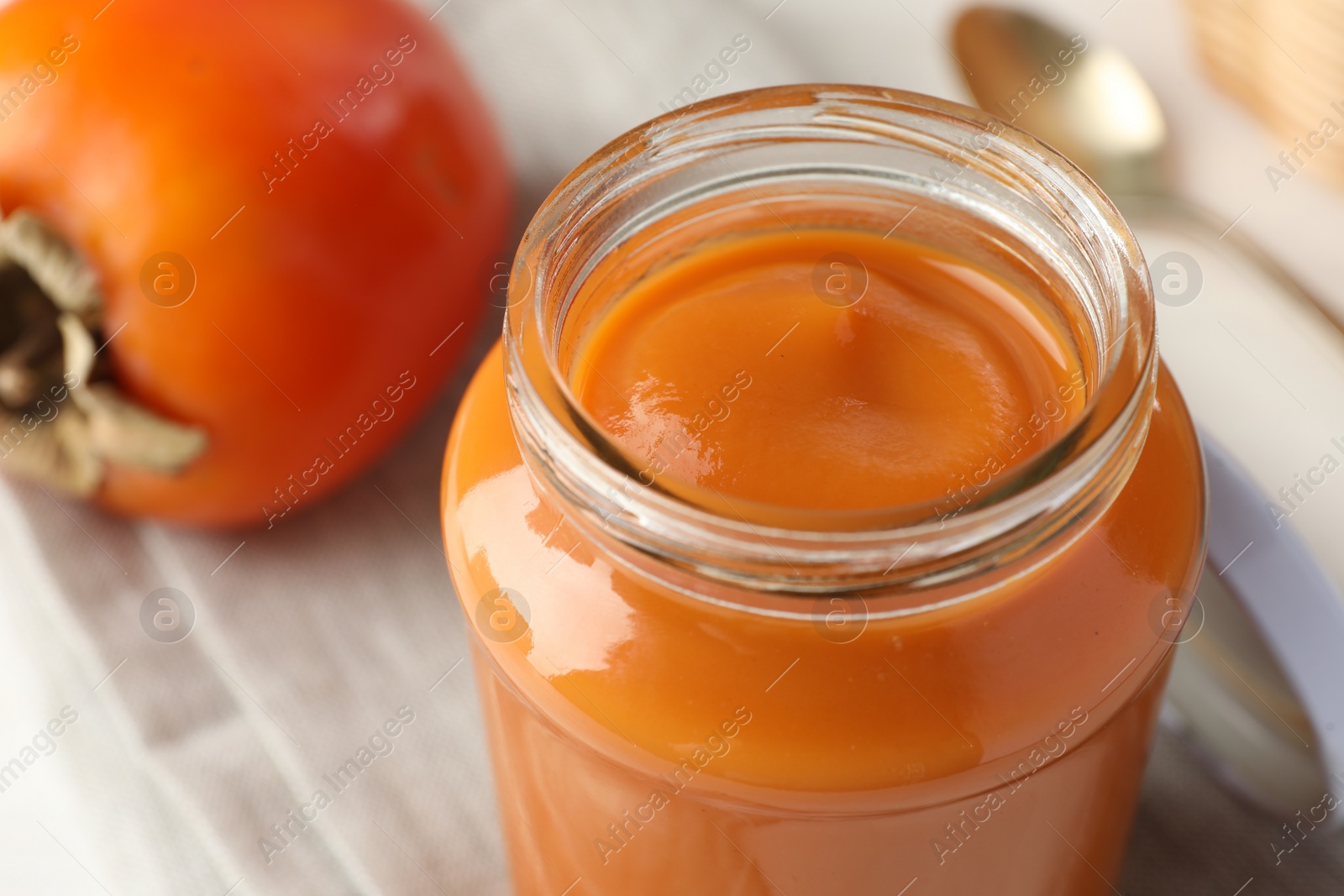 Photo of Delicious persimmon jam in glass jar and fresh fruit on table, closeup