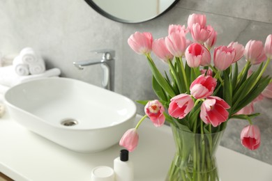 Photo of Vase with beautiful pink tulips near sink in bathroom, closeup