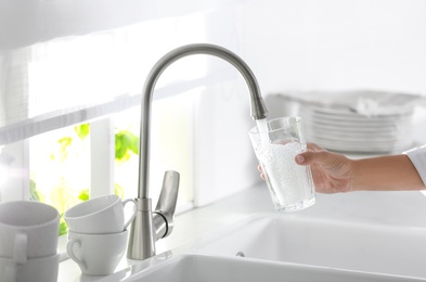 Photo of Woman pouring water into glass in kitchen, closeup