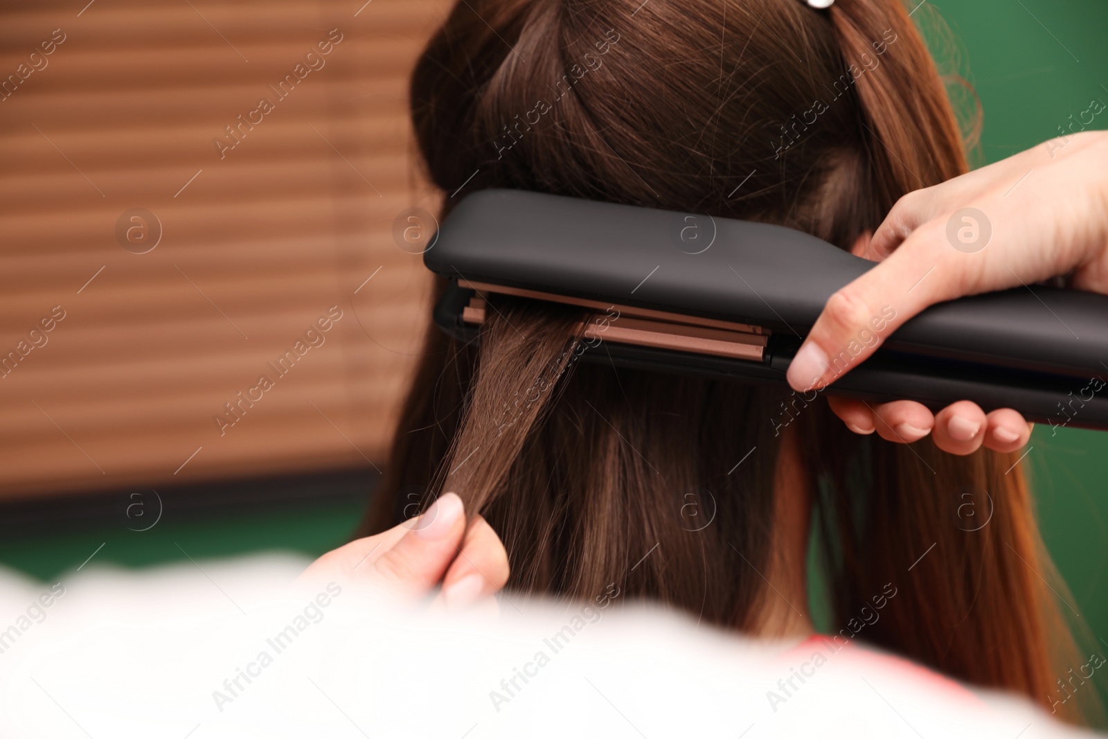 Photo of Stylist straightening woman's hair with flat iron in salon