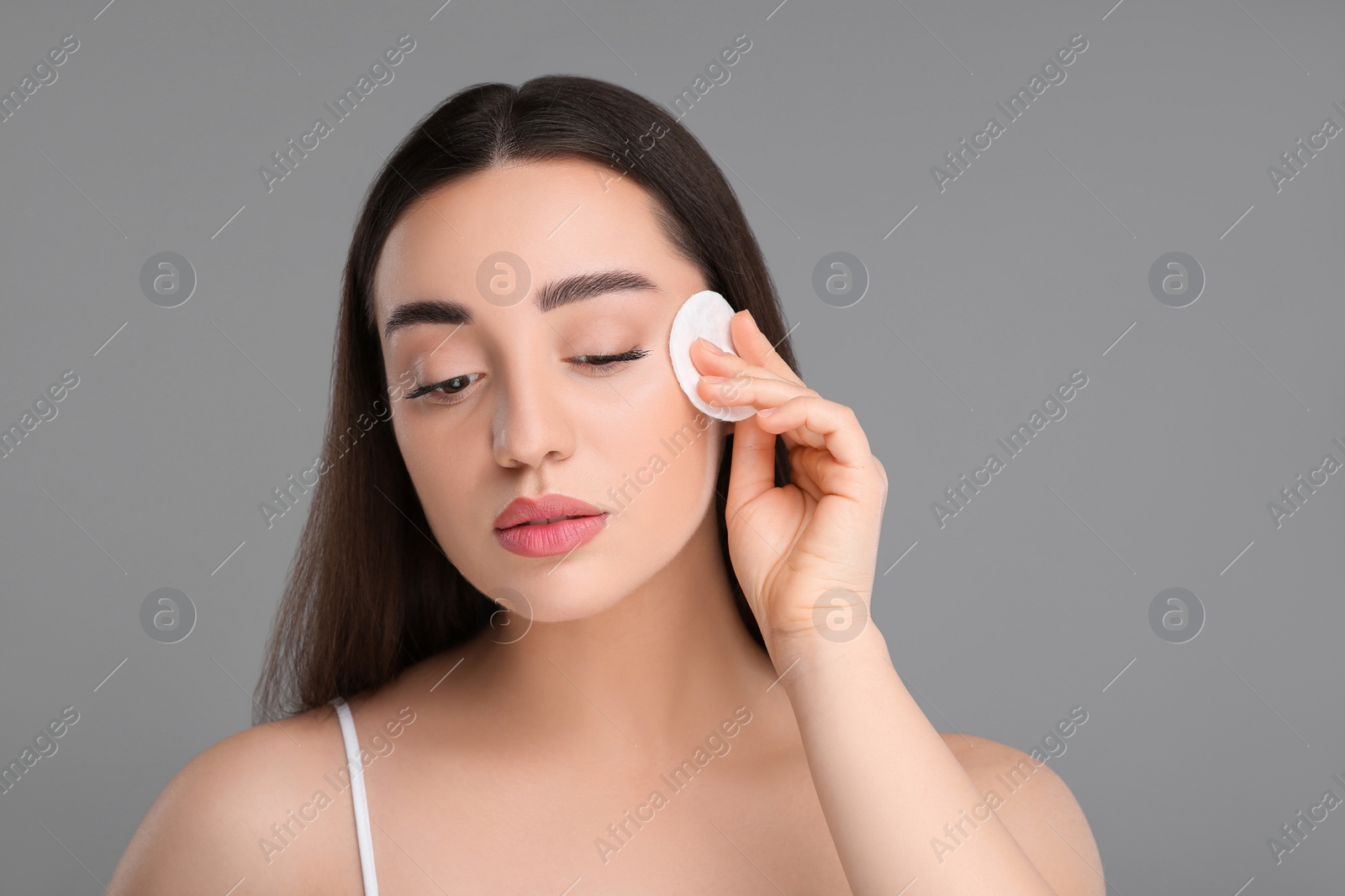 Photo of Beautiful woman removing makeup with cotton pad on gray background