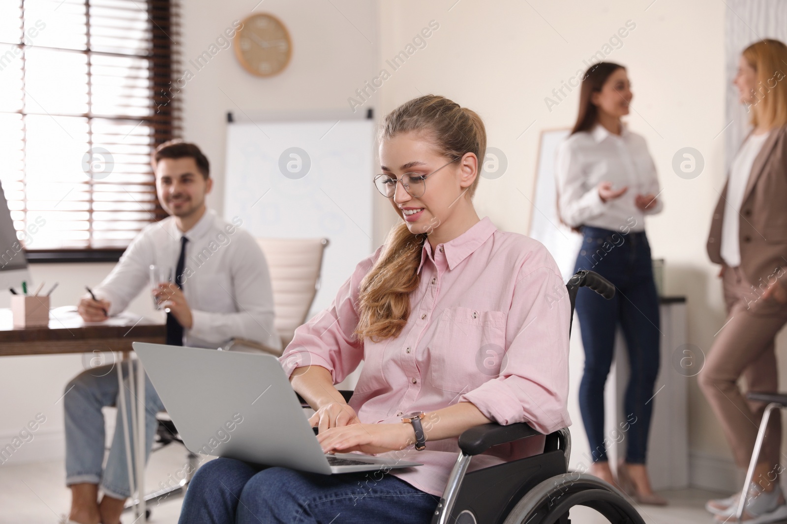 Photo of Portrait of woman in wheelchair with laptop and her colleagues at workplace
