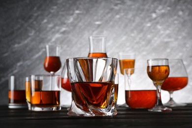 Photo of Different delicious liqueurs in glasses on dark wooden table