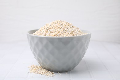 Photo of Dry barley groats in bowl on white tiled table, closeup