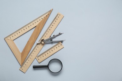 Different rulers, magnifying glass and compass on light grey background, flat lay. Space for text