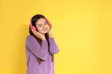 Photo of Attractive young woman enjoying music in headphones on color background. Space for text