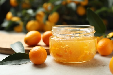 Delicious kumquat jam in jar and fresh fruits on light grey table, space for text