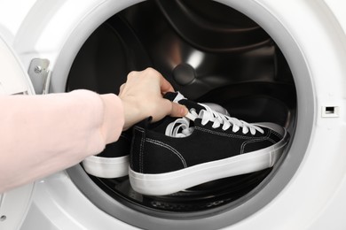 Photo of Woman putting stylish sneakers into washing machine, closeup