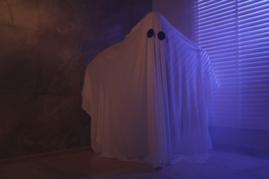 Photo of Creepy ghost. Woman covered with sheet near window in color lights