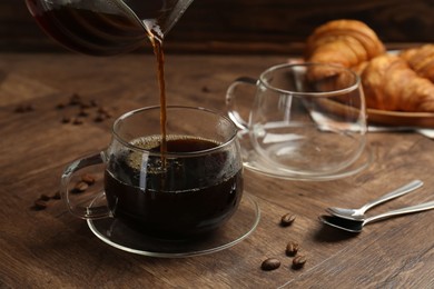 Photo of Pouring coffee into glass cup at wooden table, closeup