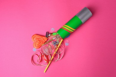 Photo of Party cracker and different festive items on bright pink background, flat lay