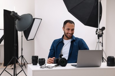 Photo of Young professional photographer with camera working on laptop in modern photo studio, space for text