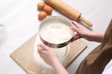Photo of Woman sieving flour at white wooden table, above view