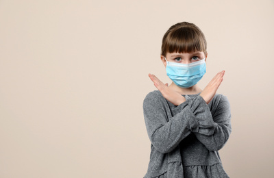 Photo of Little girl in medical mask on beige background, space for text. Virus protection