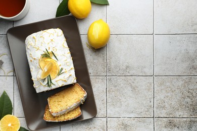 Photo of Tasty lemon cake with glaze, citrus fruits and tea on gray table, flat lay. Space for text