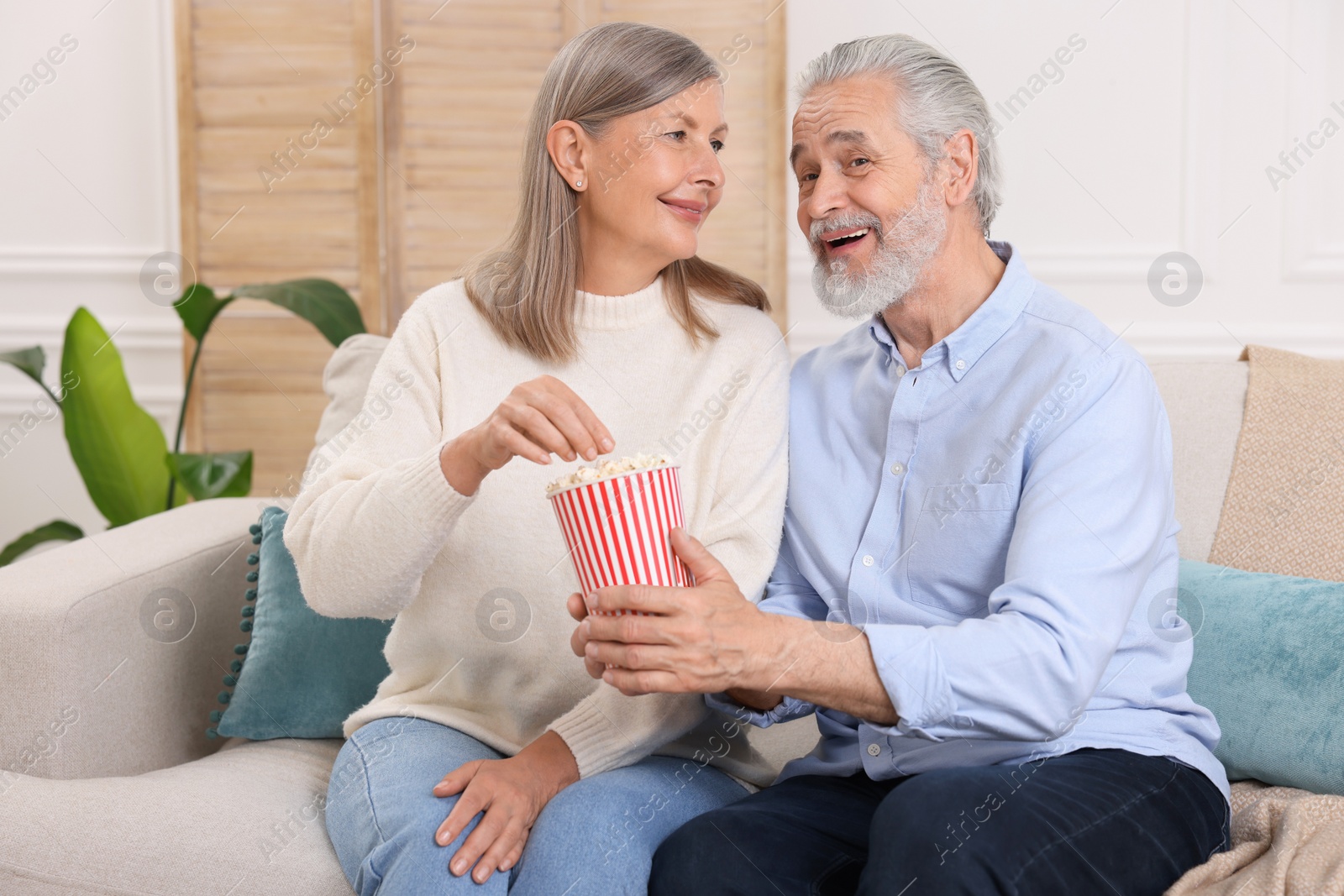 Photo of Happy senior couple with popcorn on sofa indoors