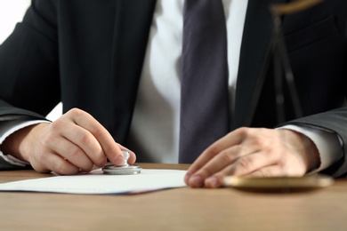Photo of Male notary stamping document at table, closeup
