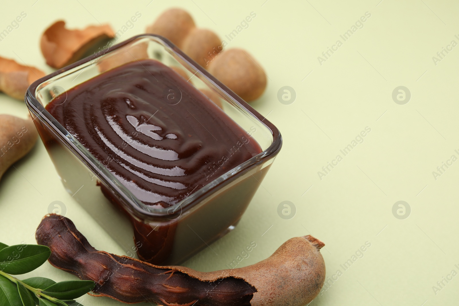 Bowl of tasty tamarind sauce, leaves and fresh pods on light green table. Space for text Photo of Bowl of tasty tamarind sauce, leaves and fresh pods on light green table. Space for text