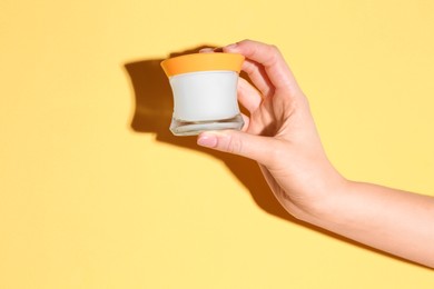 Photo of Woman holding jar of cream on yellow background, closeup