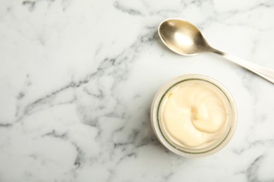 Photo of Jar of delicious mayonnaise and spoon on white marble table, flat lay. Space for text
