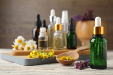 Photo of Bottles of different essential oils and wildflowers on wooden table, space for text